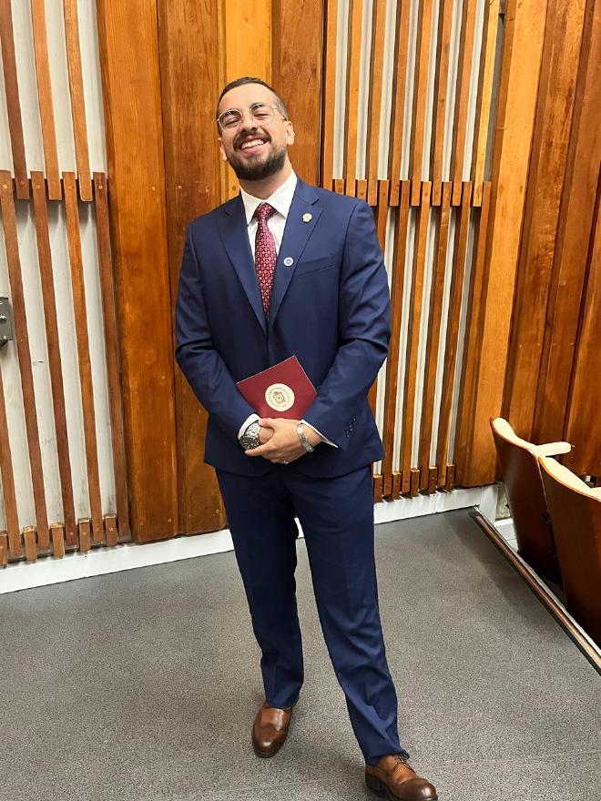 Daniel Felipe Montenegro smiling in a navy suit, holding a diploma folder on graduation day