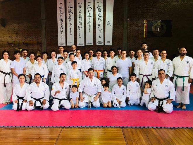 Club Chrysler karatekas of all ages in white gis, posing on the tatami with the Dojo Kun banners behind them
