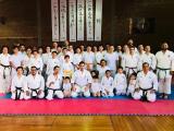 Club Chrysler karatekas of all ages in white gis, posing on the tatami with the Dojo Kun banners behind them