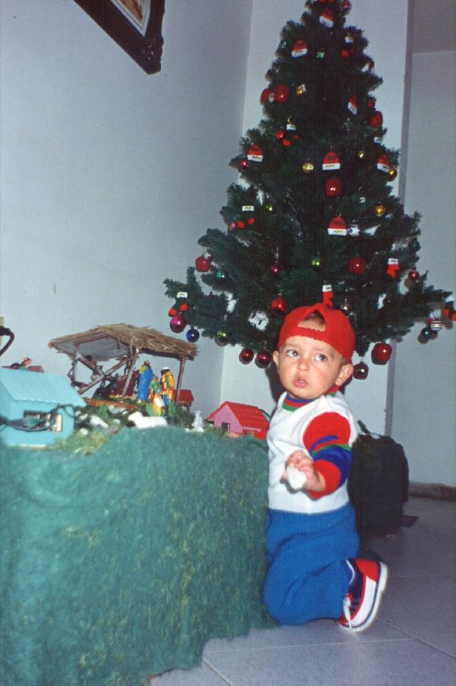 Daniel Felipe Montenegro as a toddler in a red hat, kneeling beside the Christmas tree and the nativity scene with a stolen sheep in his hand
