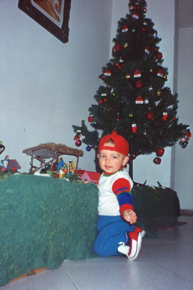Daniel Felipe Montenegro as a toddler, kneeling by the Christmas tree with a plaster sheep from the nativity scene, looking back at the camera