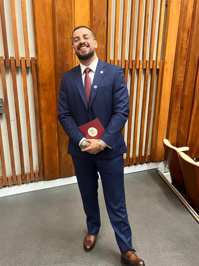 Daniel Felipe Montenegro laughing, in a navy suit, holding his diploma