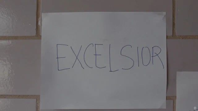 A sheet of paper taped to a tiled wall with EXCELSIOR written across it by hand